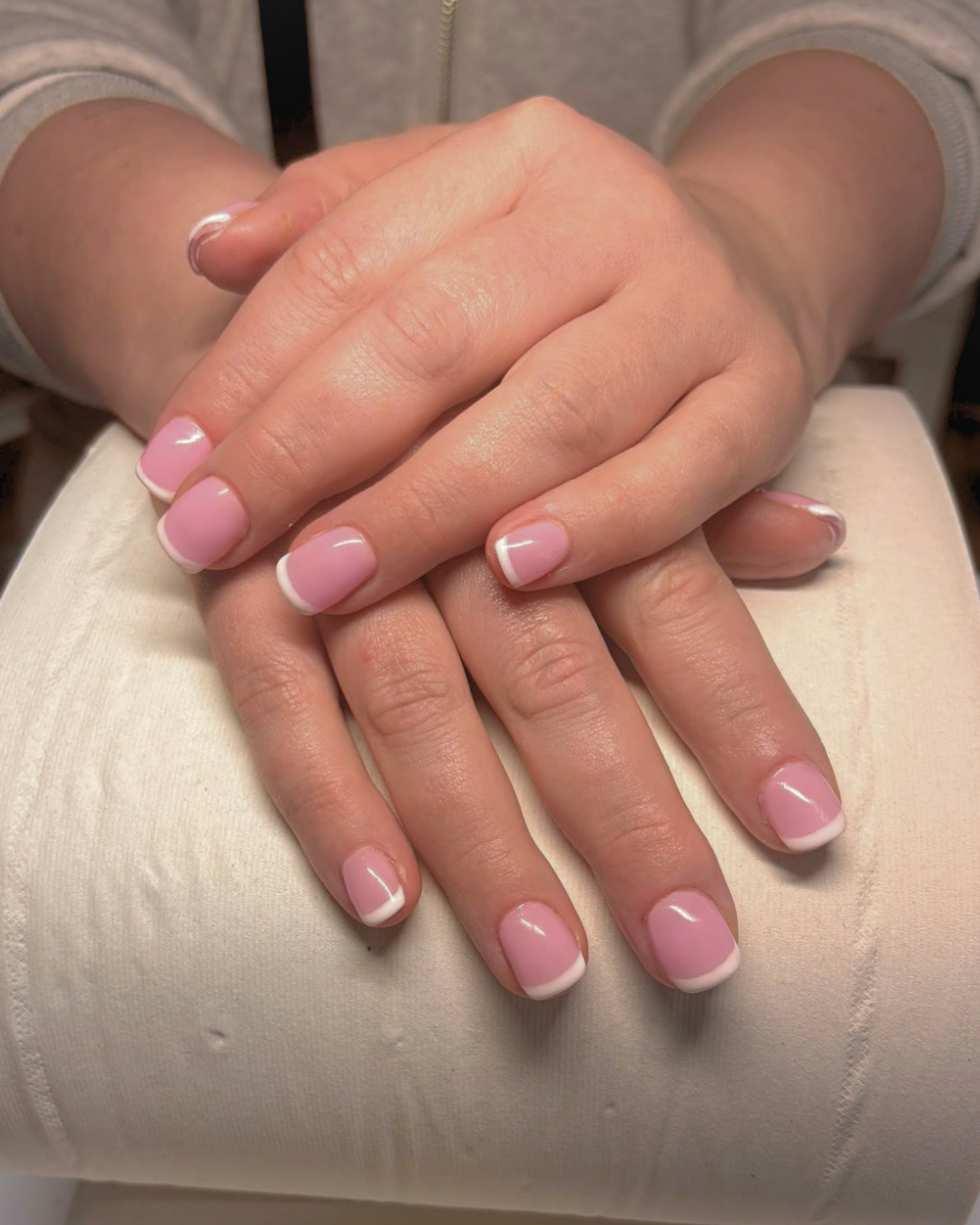 Close up of BIAB manicure with a light pink base colour and classic French tip design, short and square-shaped, the hands laying gently on a paper towel roll.