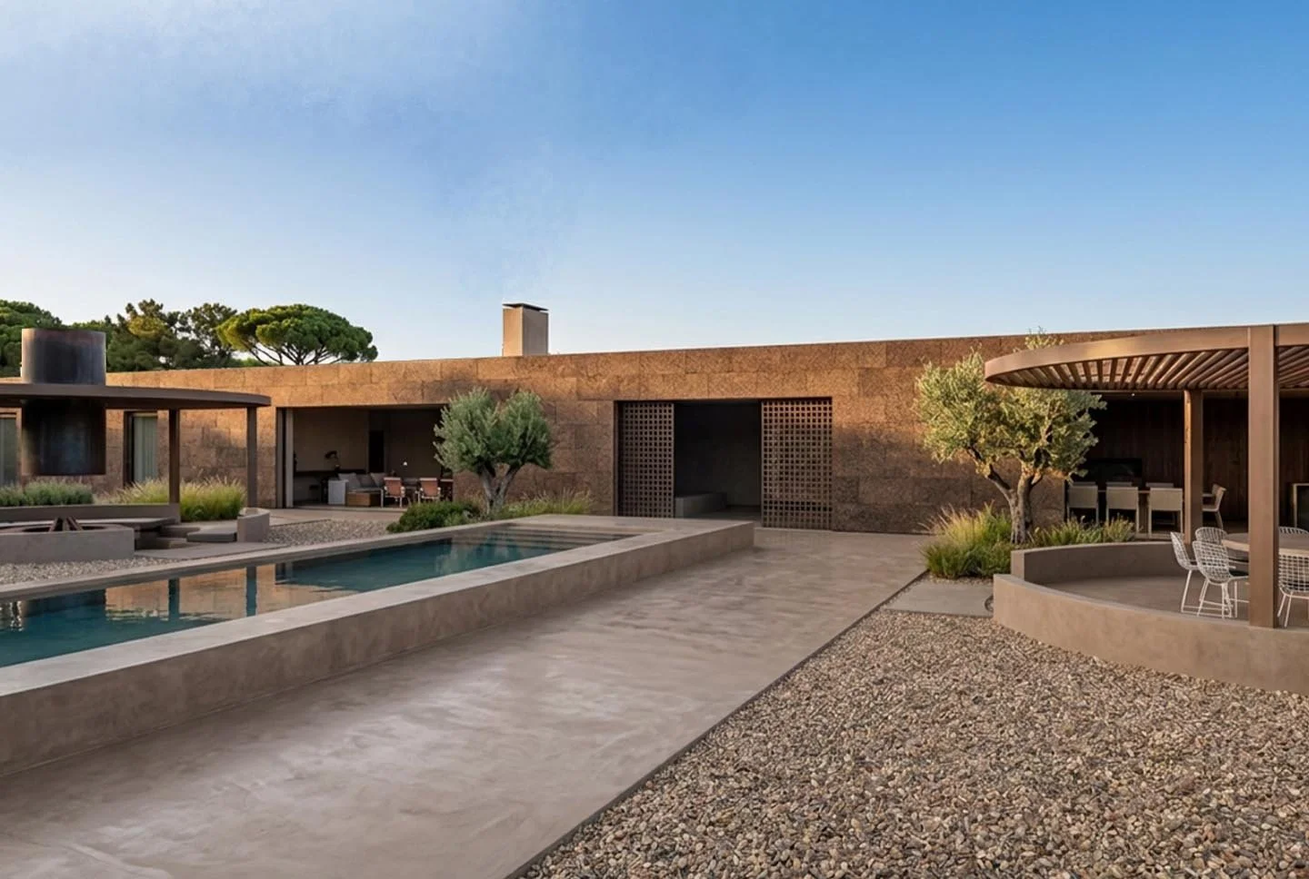 Modern outdoor patio with a rectangular pool, seating areas, and trees in a desert landscape