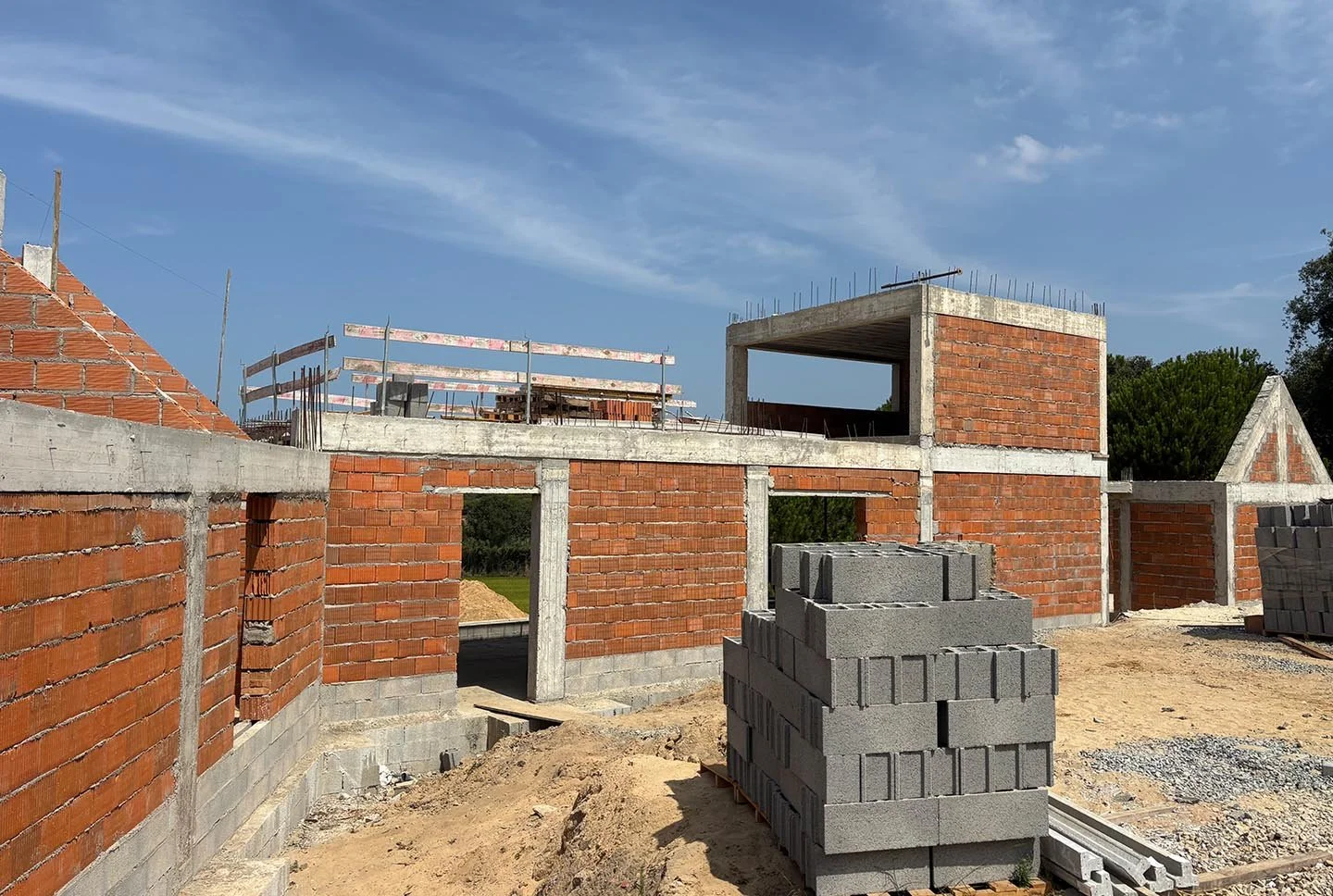 Under-construction brick building with concrete beams, grey cinder blocks stacked in front, and scaffolding against the blue sky.