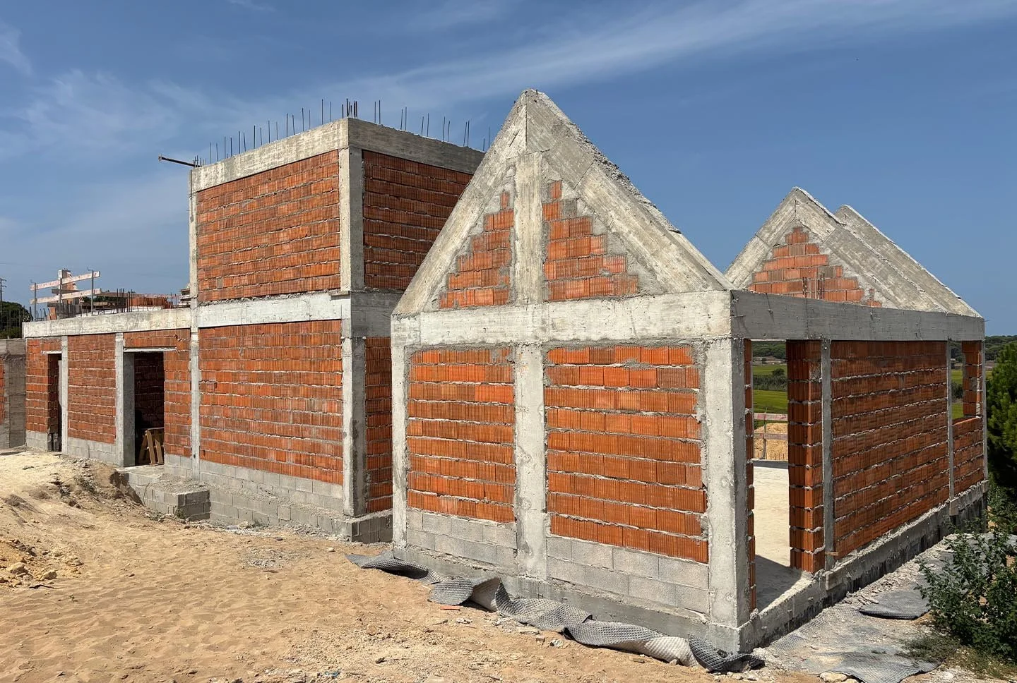unfinished brick and concrete house under construction on a dirt lot with a blue sky