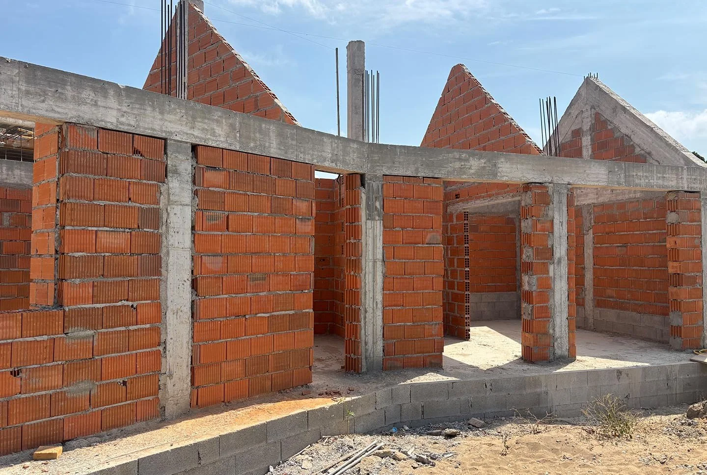 Construction site with brick walls and concrete beams being built, under a partly cloudy sky.