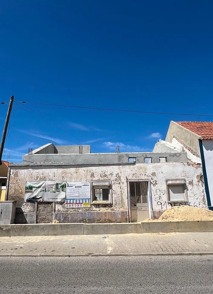 An old, weathered building under renovation with scaffolding and construction signs, next to a paved street, with a blue sky overhead.