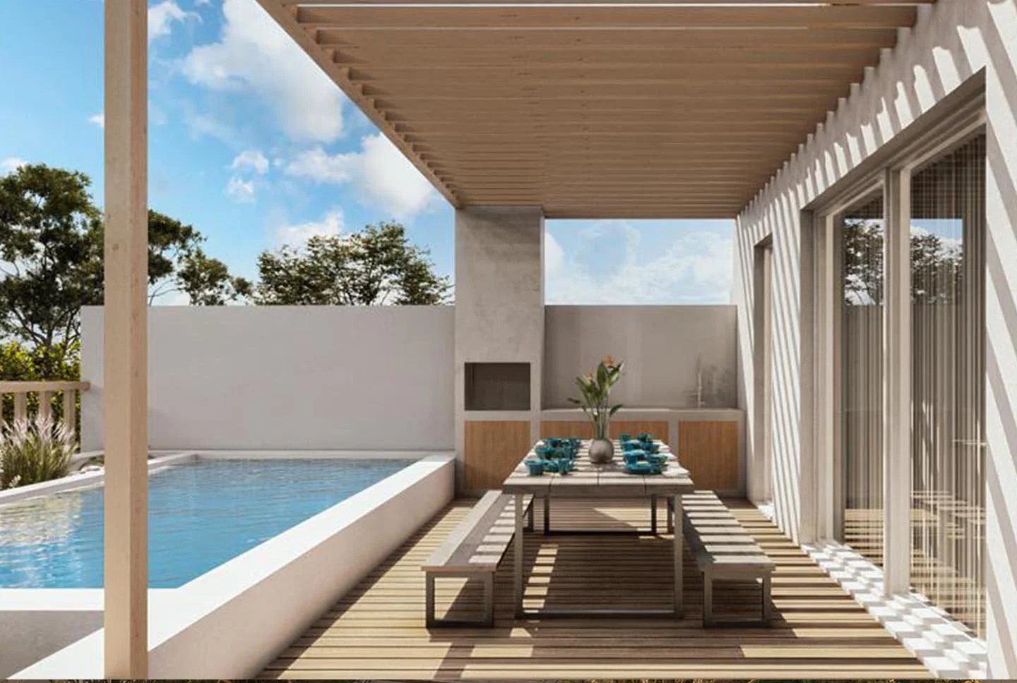 Outdoor patio with a swimming pool, dining table with benches, and a vase with flowers, under a wooden pergola, with a white wall and trees in the background.