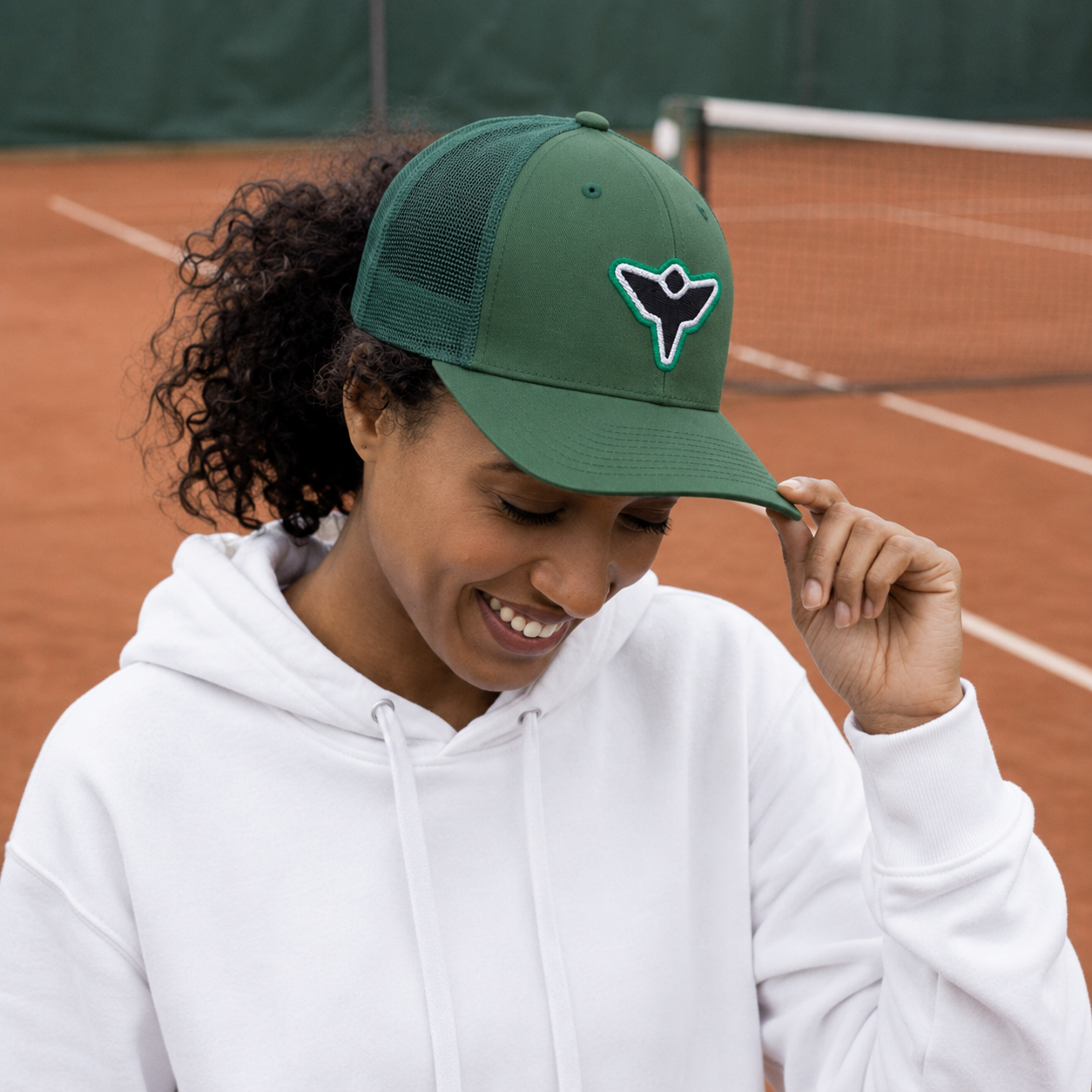 Woman wearing green cap on clay court.png