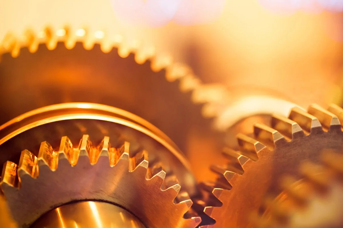 Close-up of interlocking metal gears with a warm, golden hue.