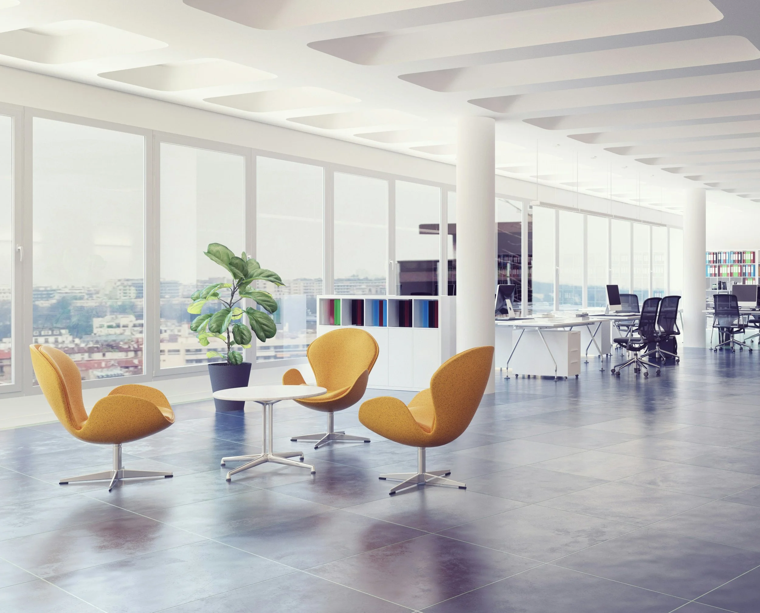 Modern office space with large windows, yellow chairs around small white tables, a white bookshelf with colorful books, potted plant, and several desks with computers in the background where Aimee Cohen of Alpha Consulting might meet with a client.