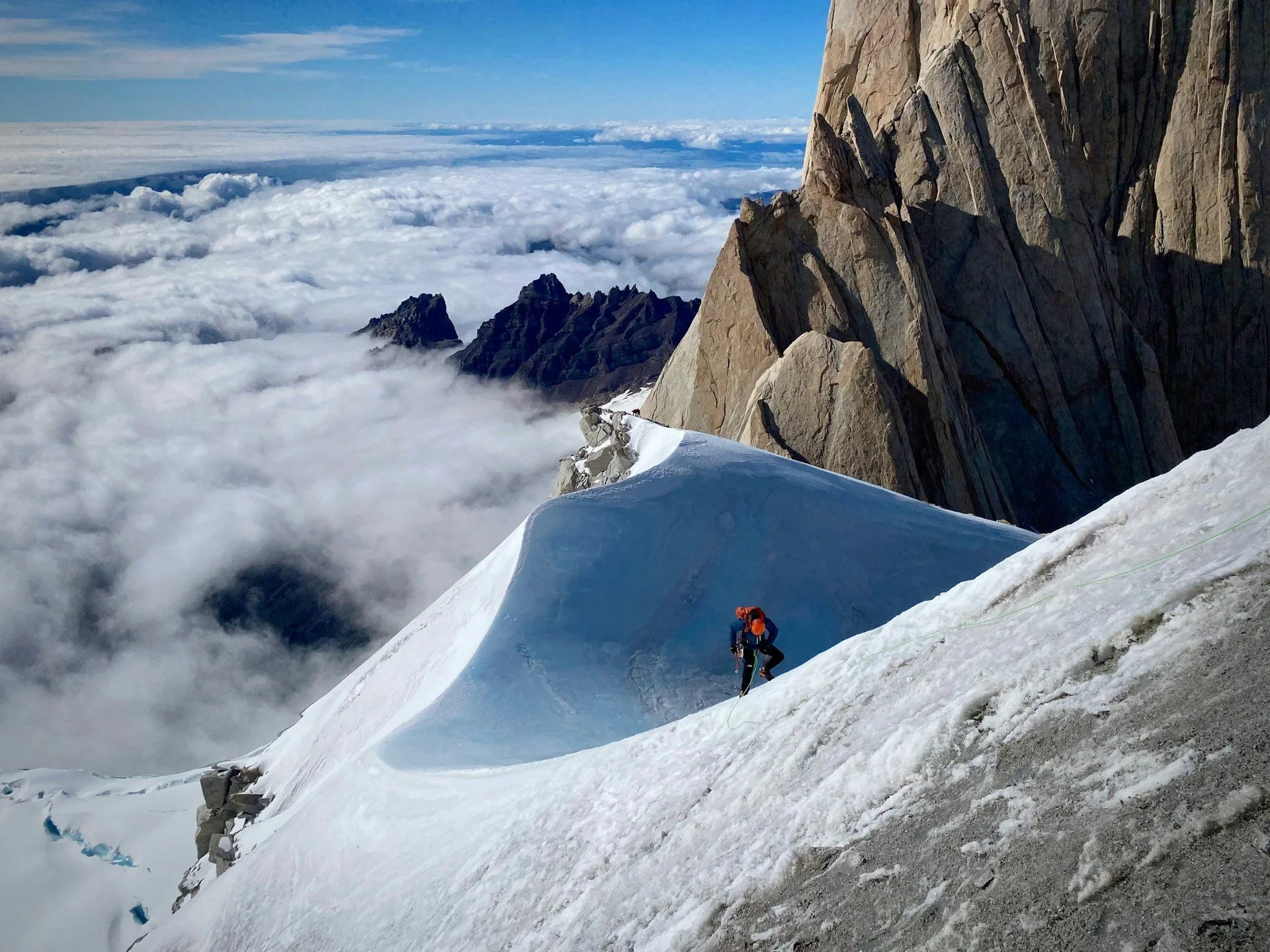 Montagne enneigée avec deux alpinistes escaladant la pente, ciel bleu avec nuages en dessous