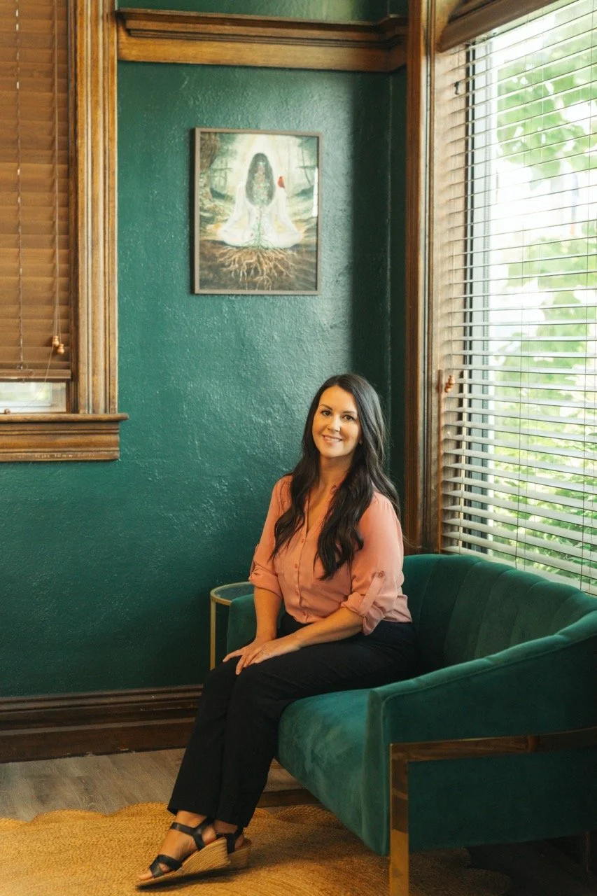 woman with brown hair and a pink shirt sitting on a green couch with a dark green wall behind her