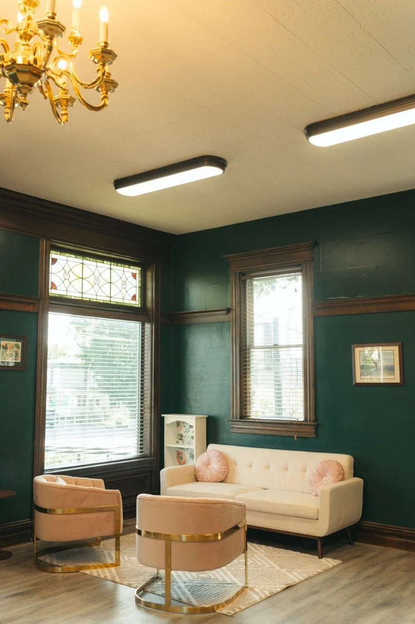 two rose pink chairs across from a white couch with a dark green wall behind it