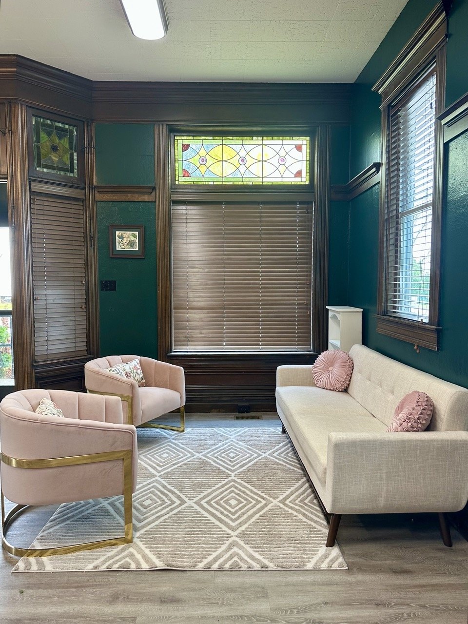 two pink chairs facing a white couch with a patterned rug underneath and a dark green wall in the background