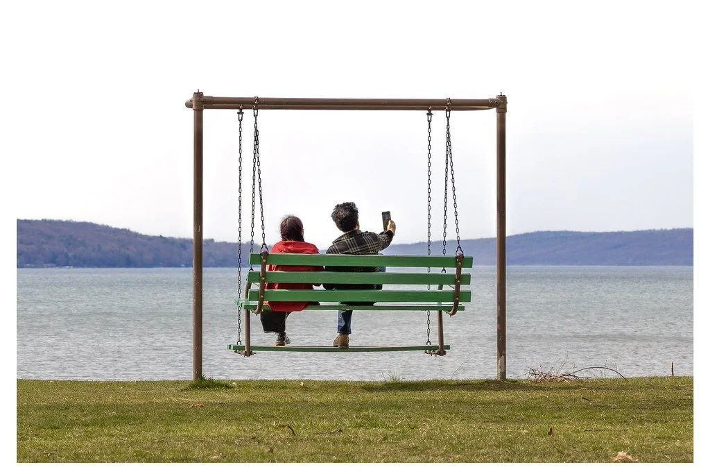 Sophie Khan, left, and her father, Matthew Khan, take a selfie while sitting on a swing bench overlooking Cayuga Lake at Stewart Park in Ithaca, New York. 