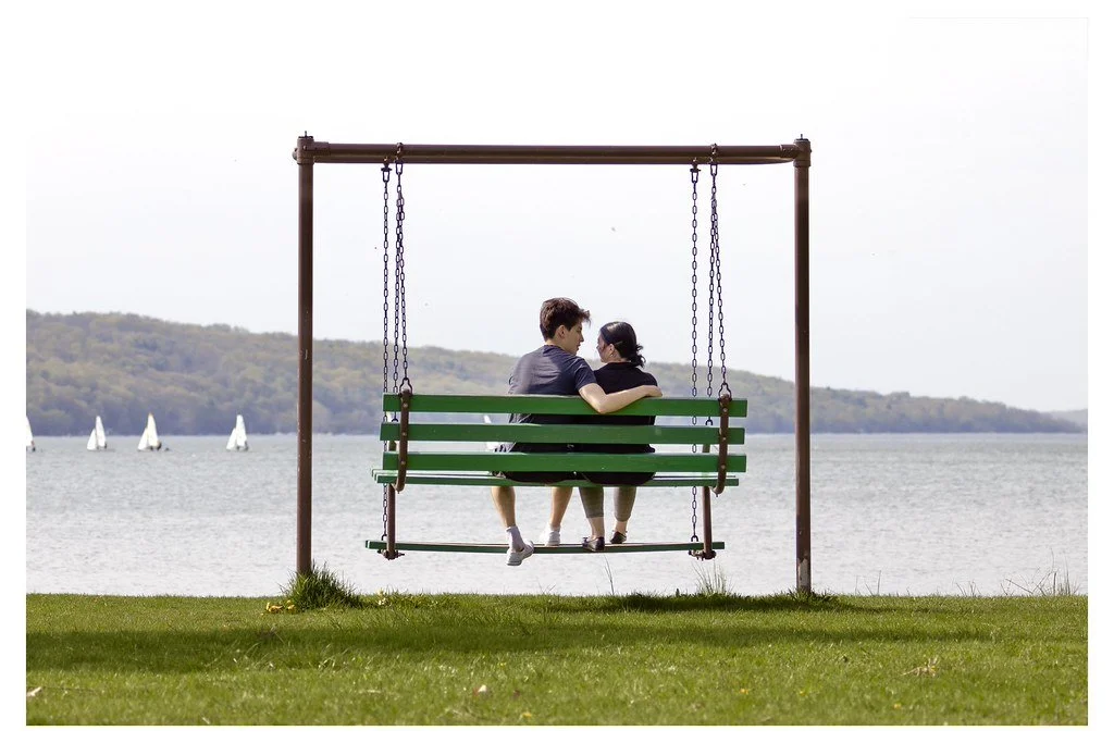 Couple Josh Rivas, left, and Nadia Boyer, sit on a swing bench overlooking Cayuga Lake at Stewart Park in Ithaca, New York. 