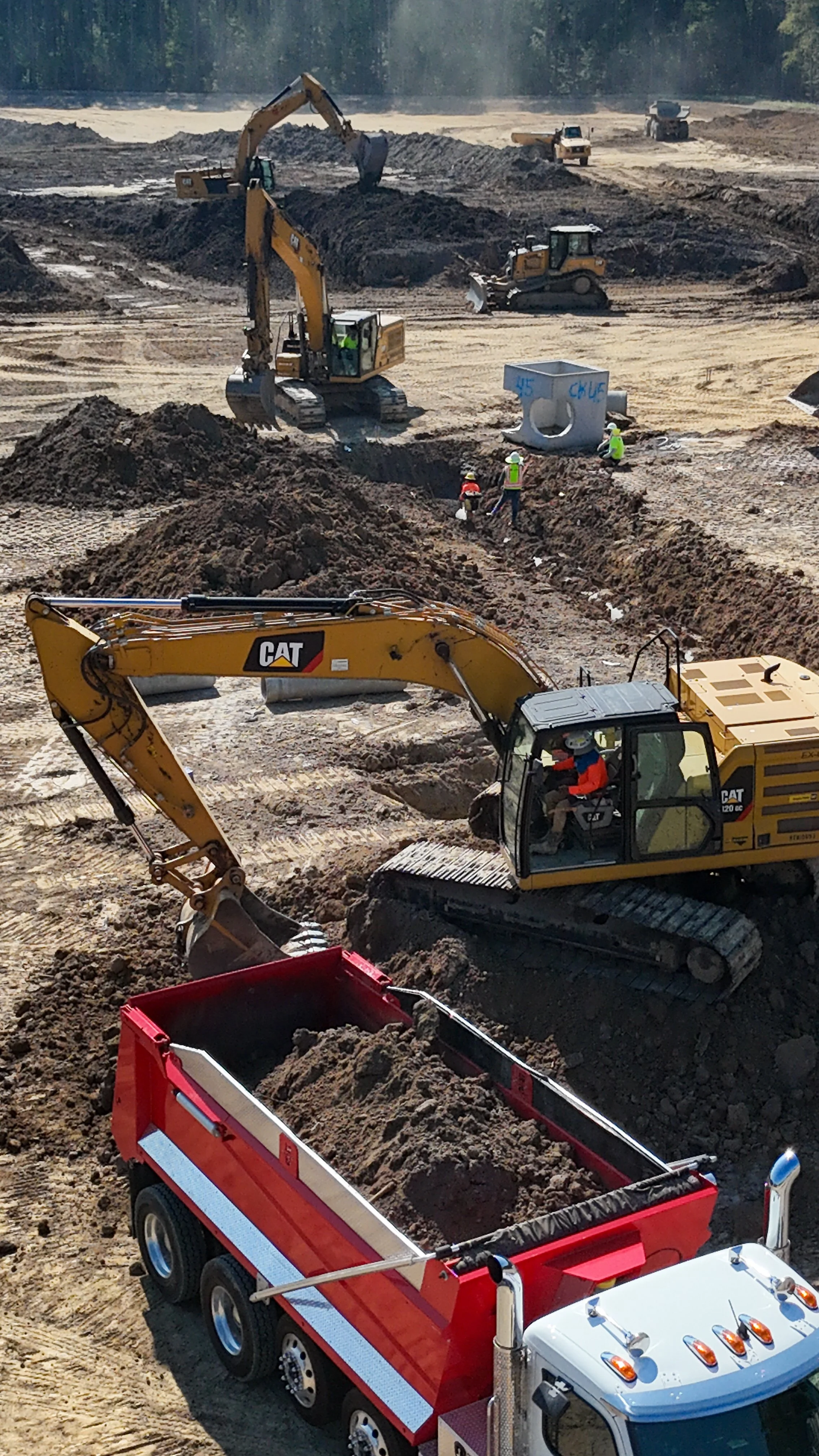 Construction site with multiple excavators and construction vehicles, and workers in safety gear working on a dirt surface.
