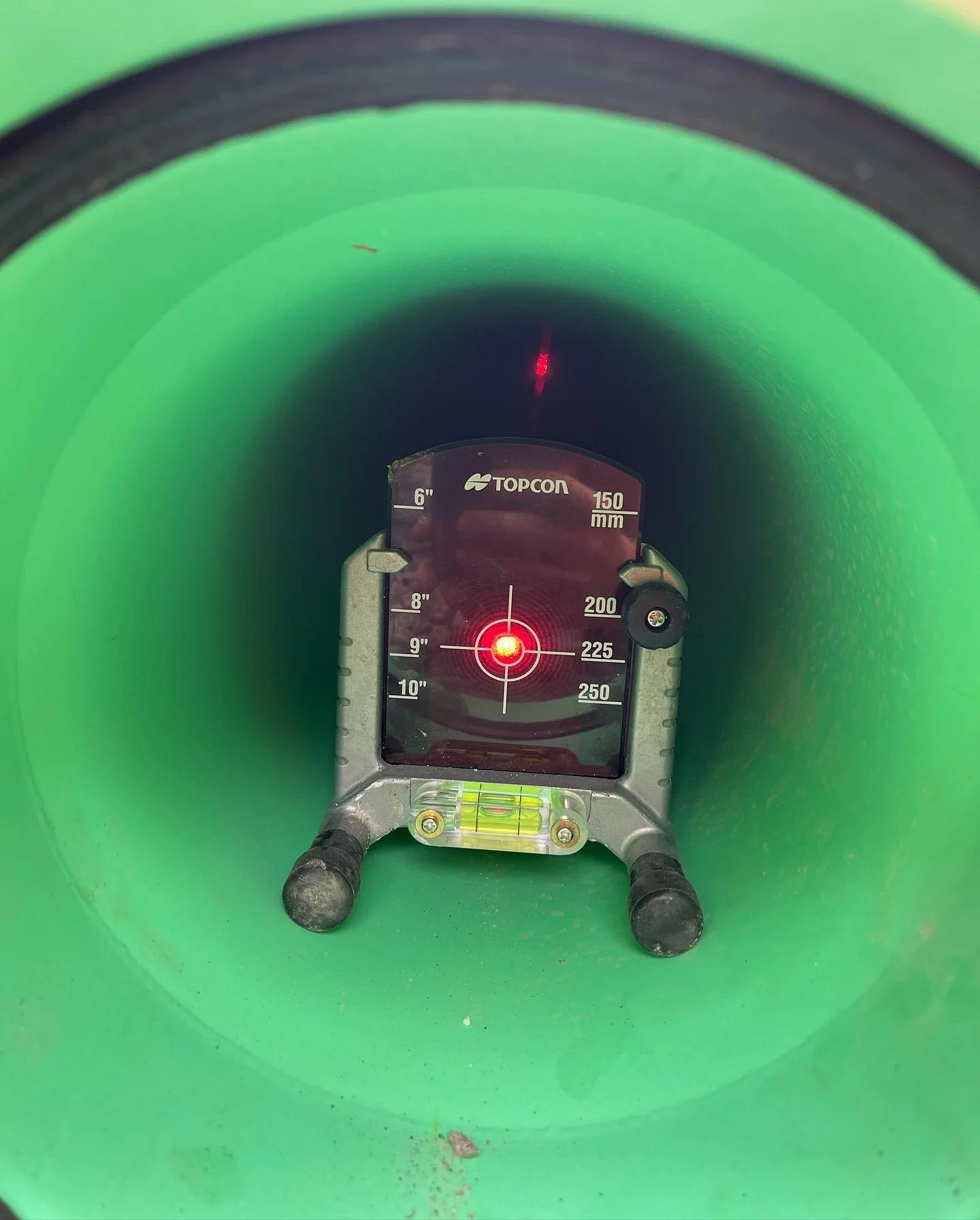 Interior view of a green pipe with a top of a laser measurement device showing measurements in inches and millimeters, resting on the bottom.
