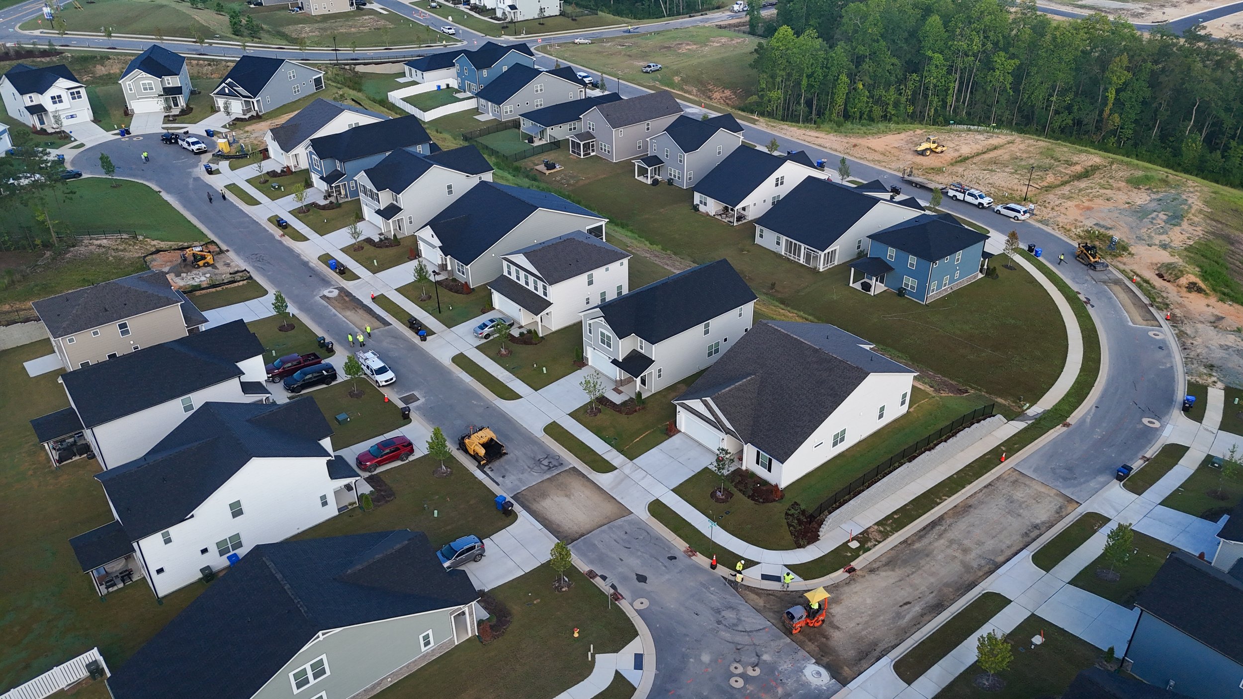 An aerial view of a new residential neighborhood with multiple houses, some under construction, and construction workers and equipment visible.