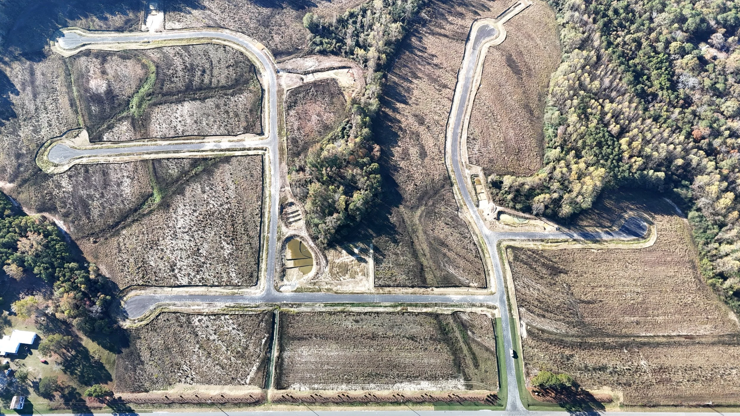 Aerial view of a winding paved road through a hilly landscape with wooded areas and ponds.