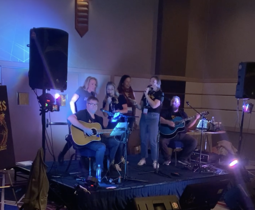 People performing music on stage with guitars and microphones, at an indoor event.