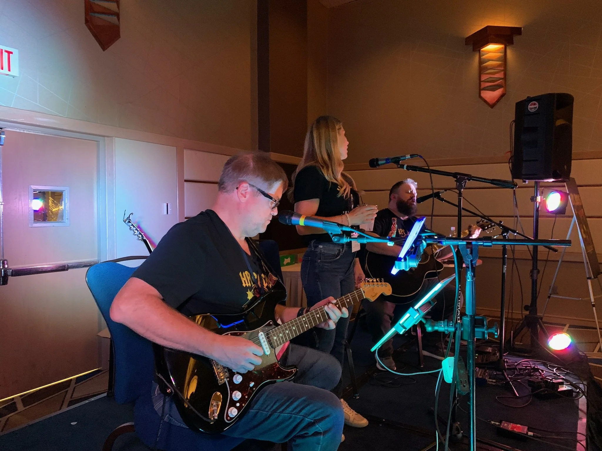 Three musicians performing on a stage, playing guitars and singing into microphones.
