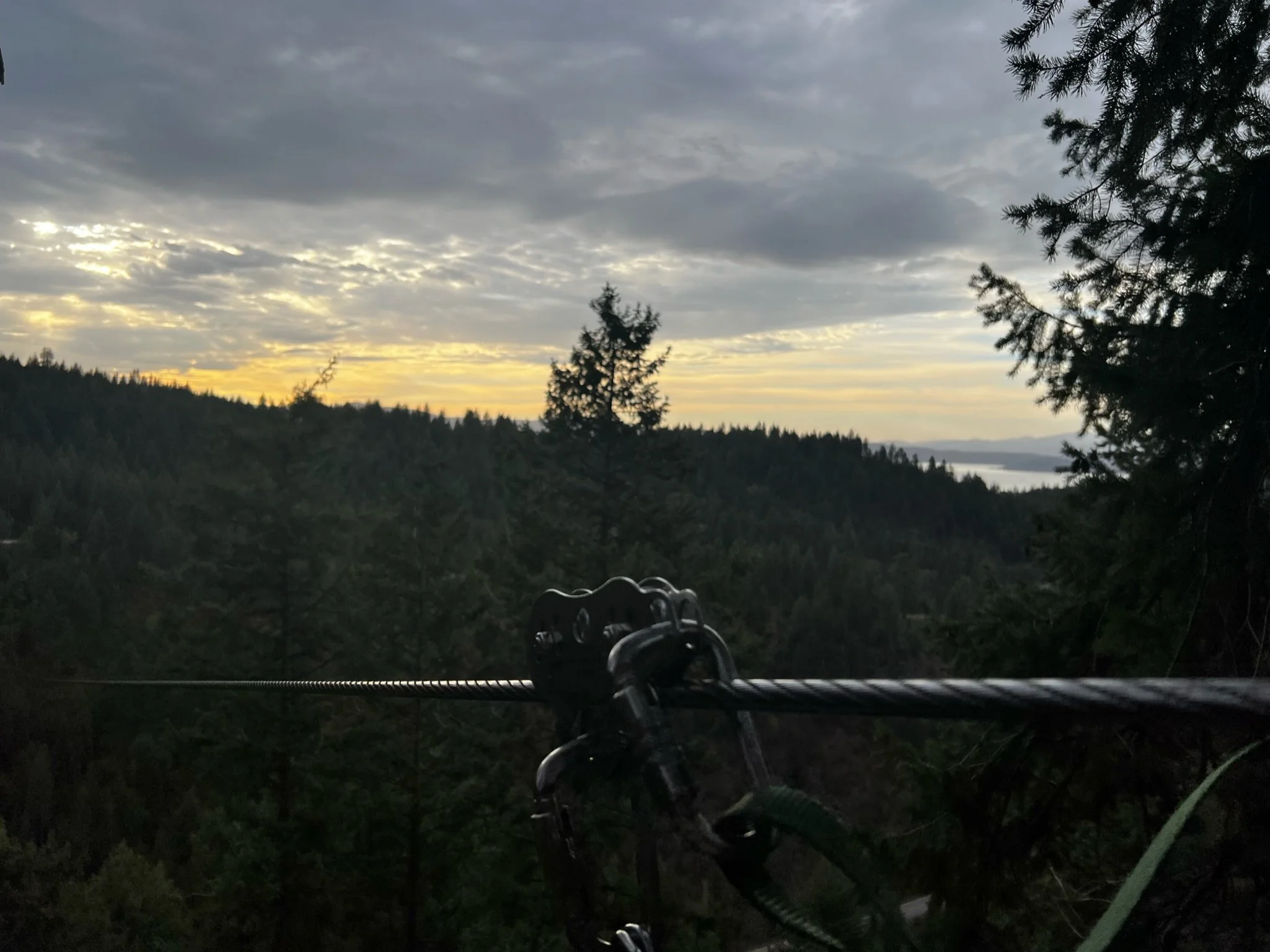 A scenic view of a sunset over a dense forest with a cable car line in the foreground.