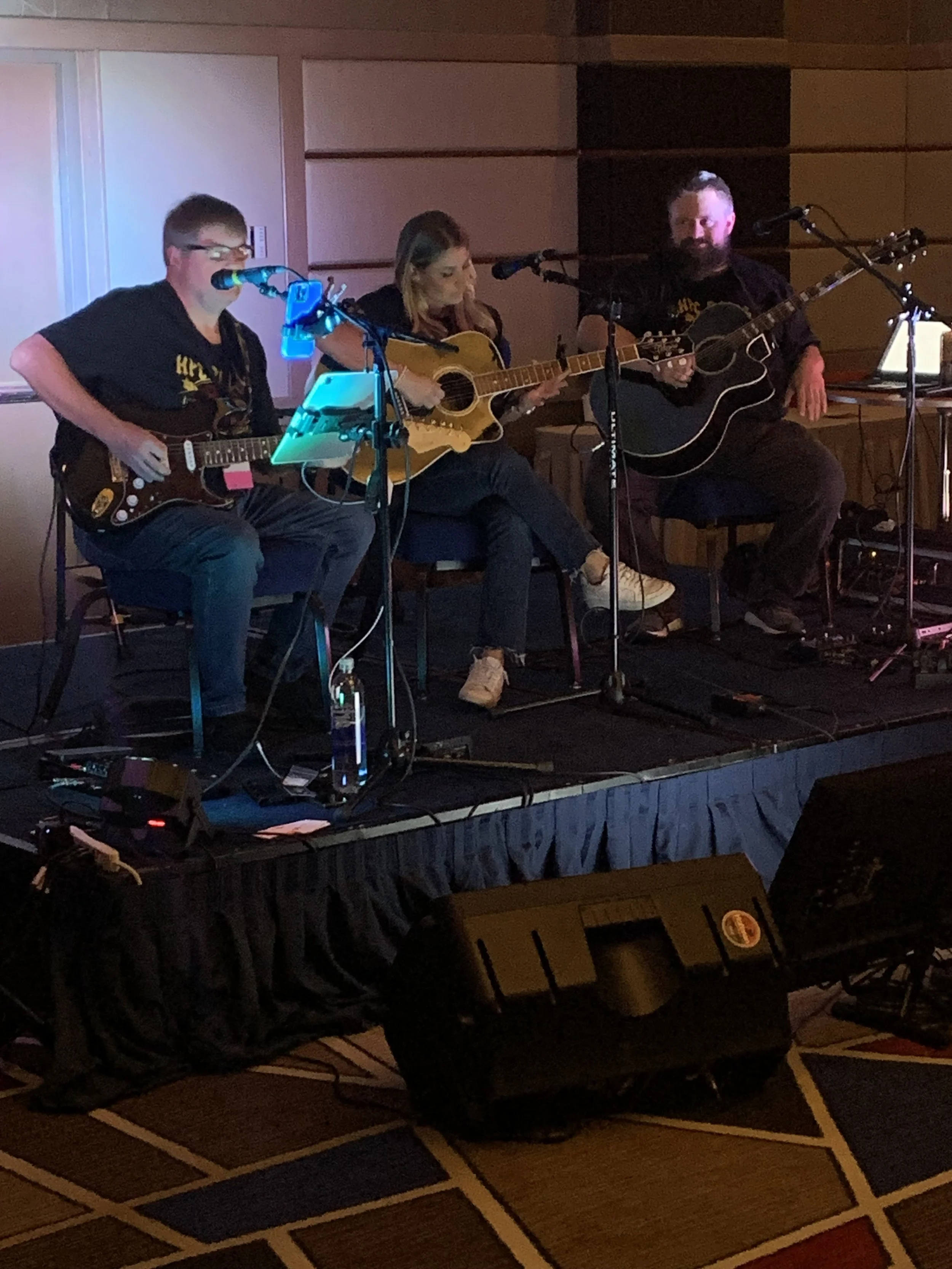 Three musicians performing on stage with guitars, microphones, and audio equipment.