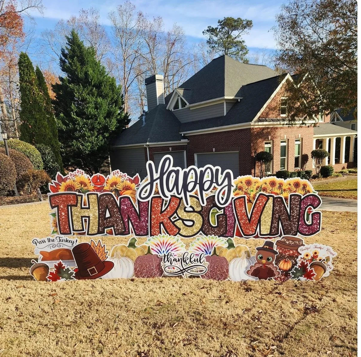 Thanksgiving outdoor sign with fall themed decorations, sunflowers, pumpkins, and cartoon turkey, in front of a house with trees and a lawn.
