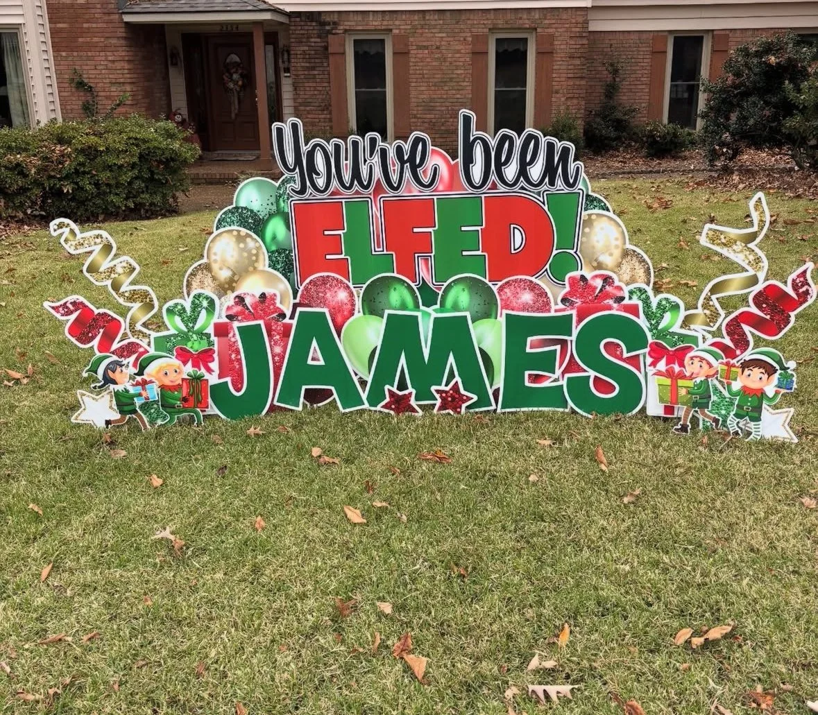 Decorative yard sign that says 'You've been ELF'd! JAMES' with Christmas-themed illustrations such as balloons, snowflakes, presents, elves, and festive ribbons, set on a lawn in front of a brick house.