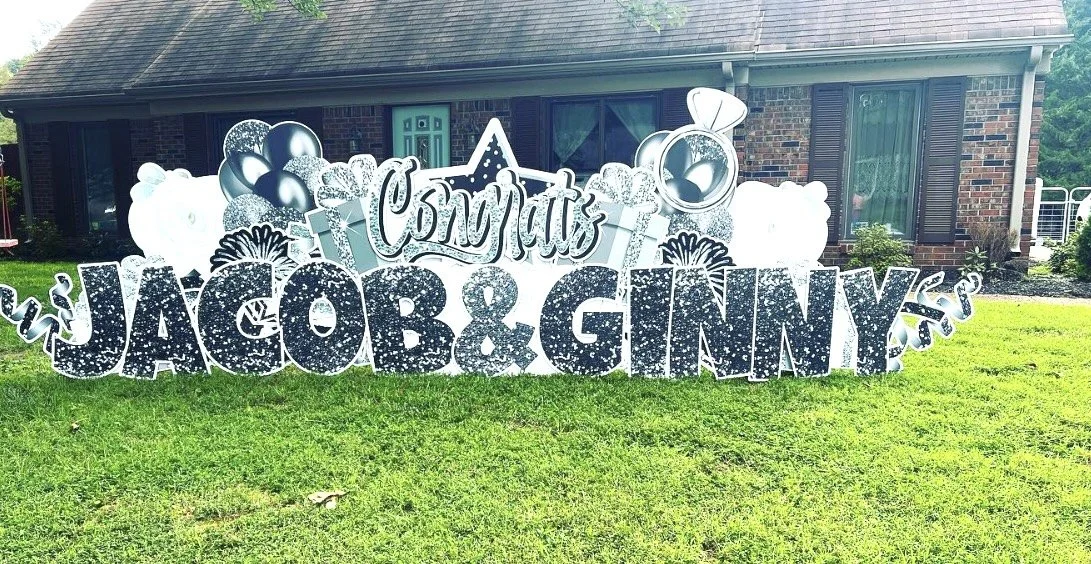 Large outdoor sign on a lawn celebrating a baby shower with balloons, stars, and the names Jacob and Ginny.
