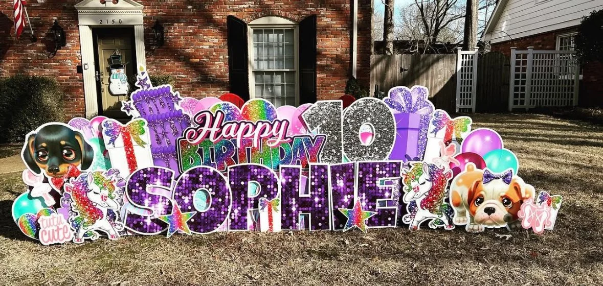 Colorful birthday yard decorations with the name 'Sophie', celebrating her 10th birthday, including balloons, unicorns, puppies, and glittery numbers, set in front of a brick house.