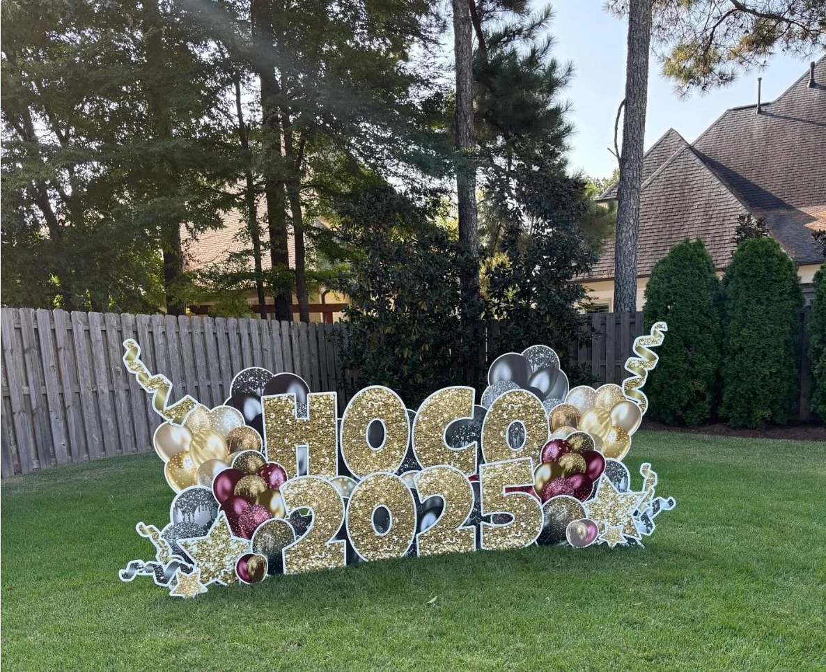 Decorative celebration display reading 'Chocolate 2025' with gold and black balloons, stars, and streamers in a backyard.