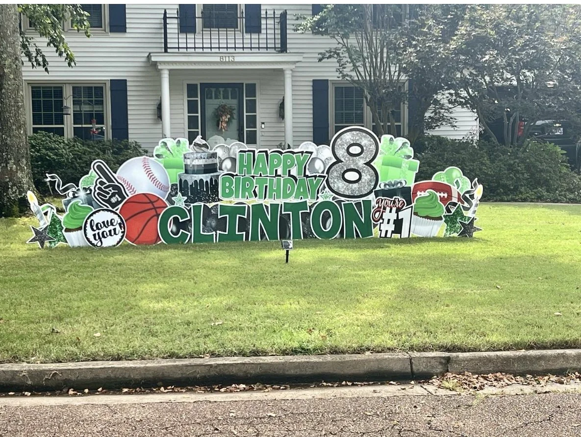 Outdoor birthday display with various decorative cutouts including a baseball, basketball, cupcakes, gift boxes, stars, and a large number 8, celebrating Clinton's 8th birthday.
