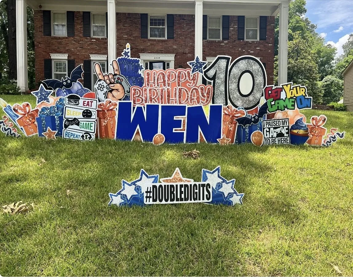 Birthday yard display with various signs and decorations, including a sign that says "Happy Birthday Wen" for a 10th birthday, with game-themed and festive elements such as bats, stars, and wrapped presents.