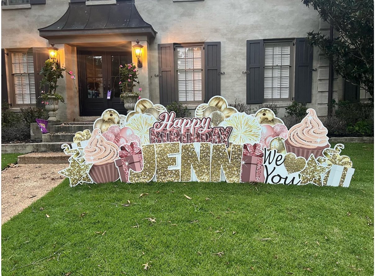 Colorful birthday decoration on a lawn with large signs reading 'Happy Birthday Jenna' and 'We Love You,' surrounded by balloons, cupcakes, gifts, and decorative elements in pink, gold, and white in front of a house with gray shutters and lit wall la