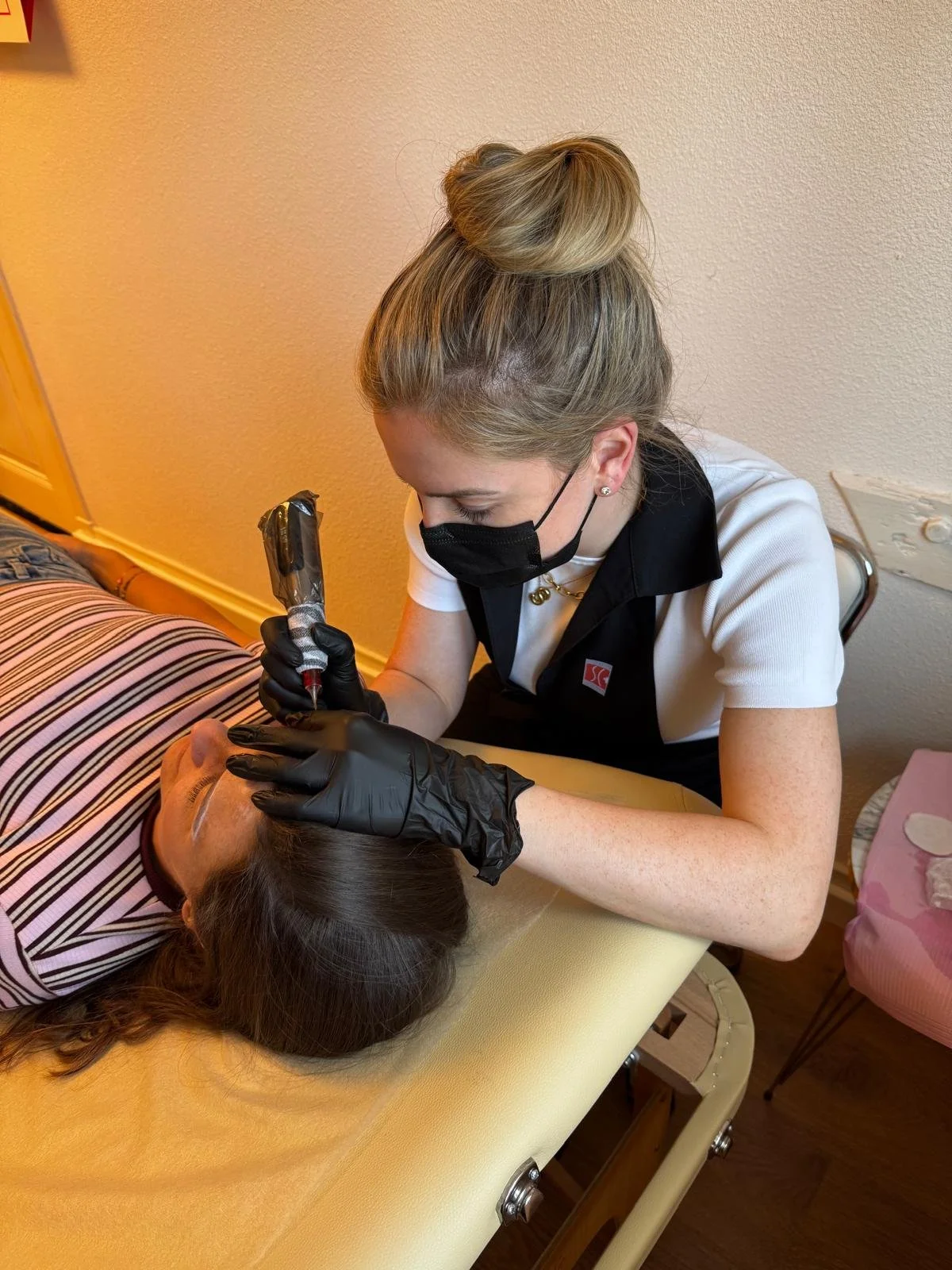Een vrouw krijgt een tatoeage gezet op haar hoofd door een tatoeëerder in een binnenruimte.