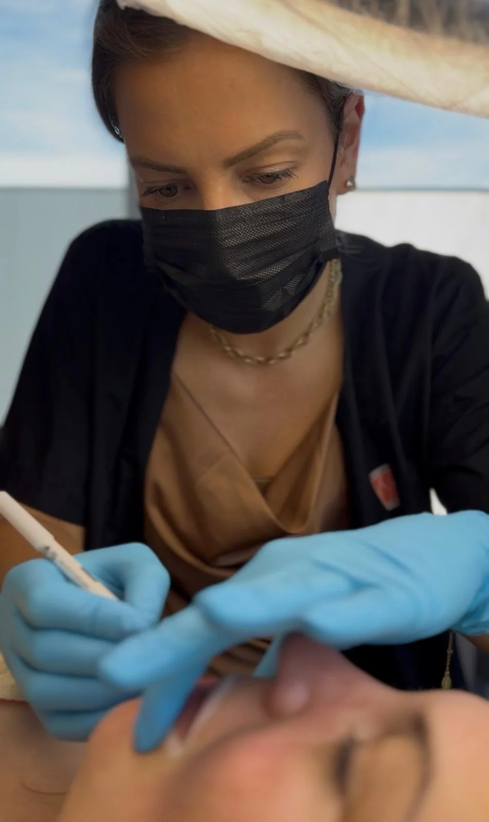 Tandarts of medisch professional die een patiënt behandelt, met een zwart mondkapje, blauwe handschoenen, die een injectie in de mond van de patiënt geeft.