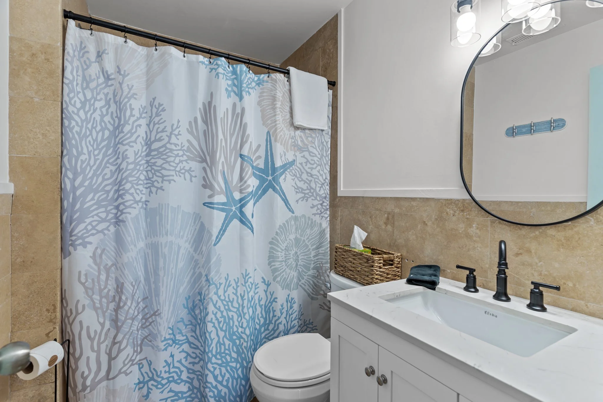 Bathroom with a shower curtain featuring a blue coral and starfish design, a bathroom sink with a white cabinet, a mirror, and a beige tiled wall.