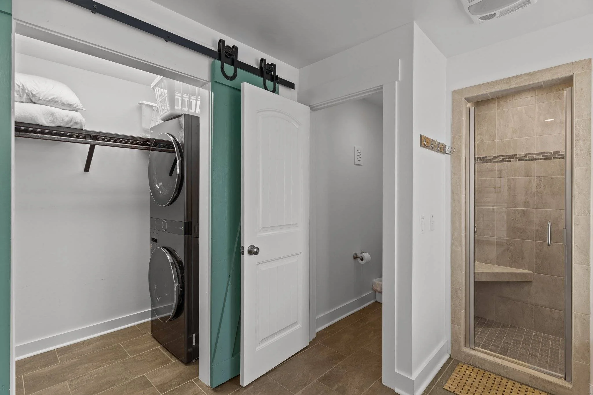 Laundry room with washer and dryer, a green sliding door, bathroom with beige tiles, and a glass shower enclosure.