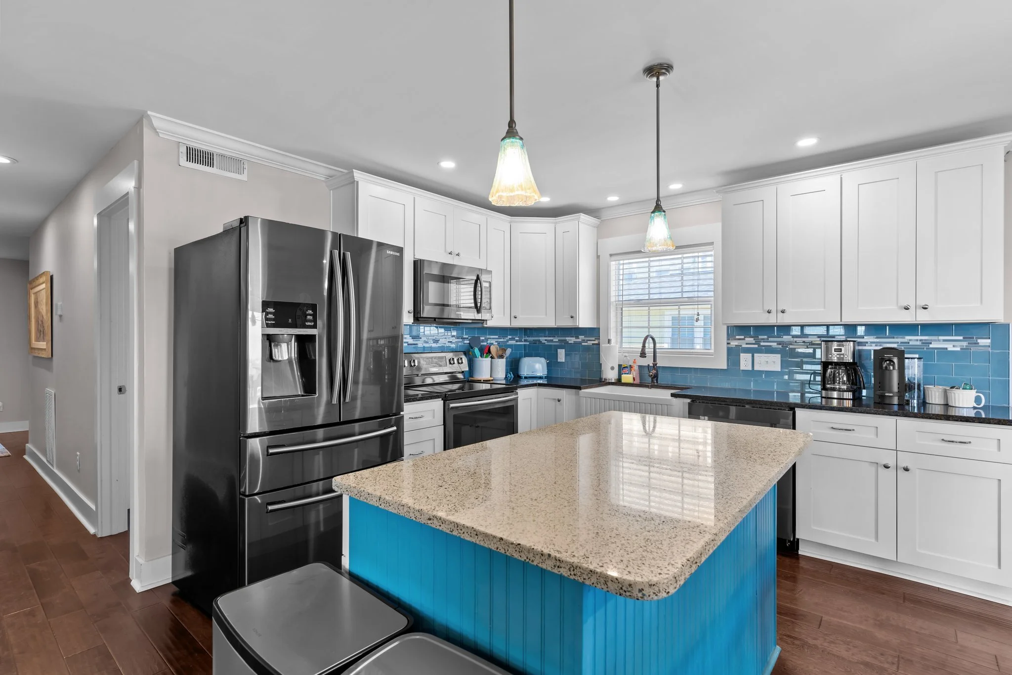 Modern kitchen with white cabinets, blue tile backsplash, granite countertops, stainless steel refrigerator and microwave, and pendant lighting.