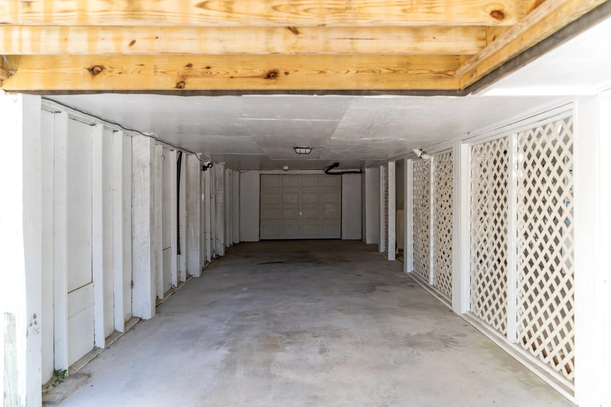 Empty garage with white walls, concrete floor, lattice side panels, and a closed garage door in the background.