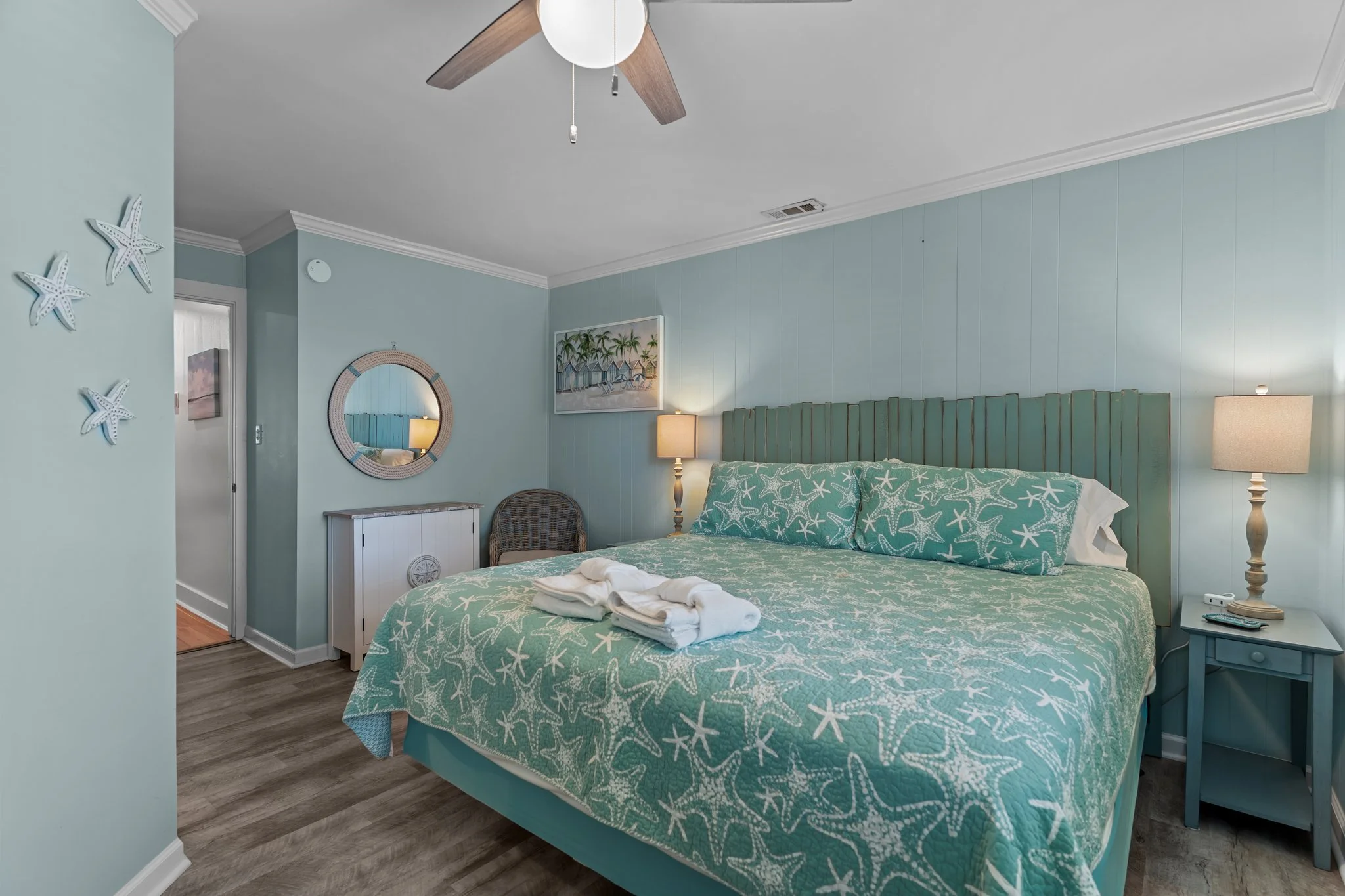 A bedroom with a starfish-themed bedding set, a bedside table with a lamp, a mirror on the wall, and beach-themed decorations on the wall.