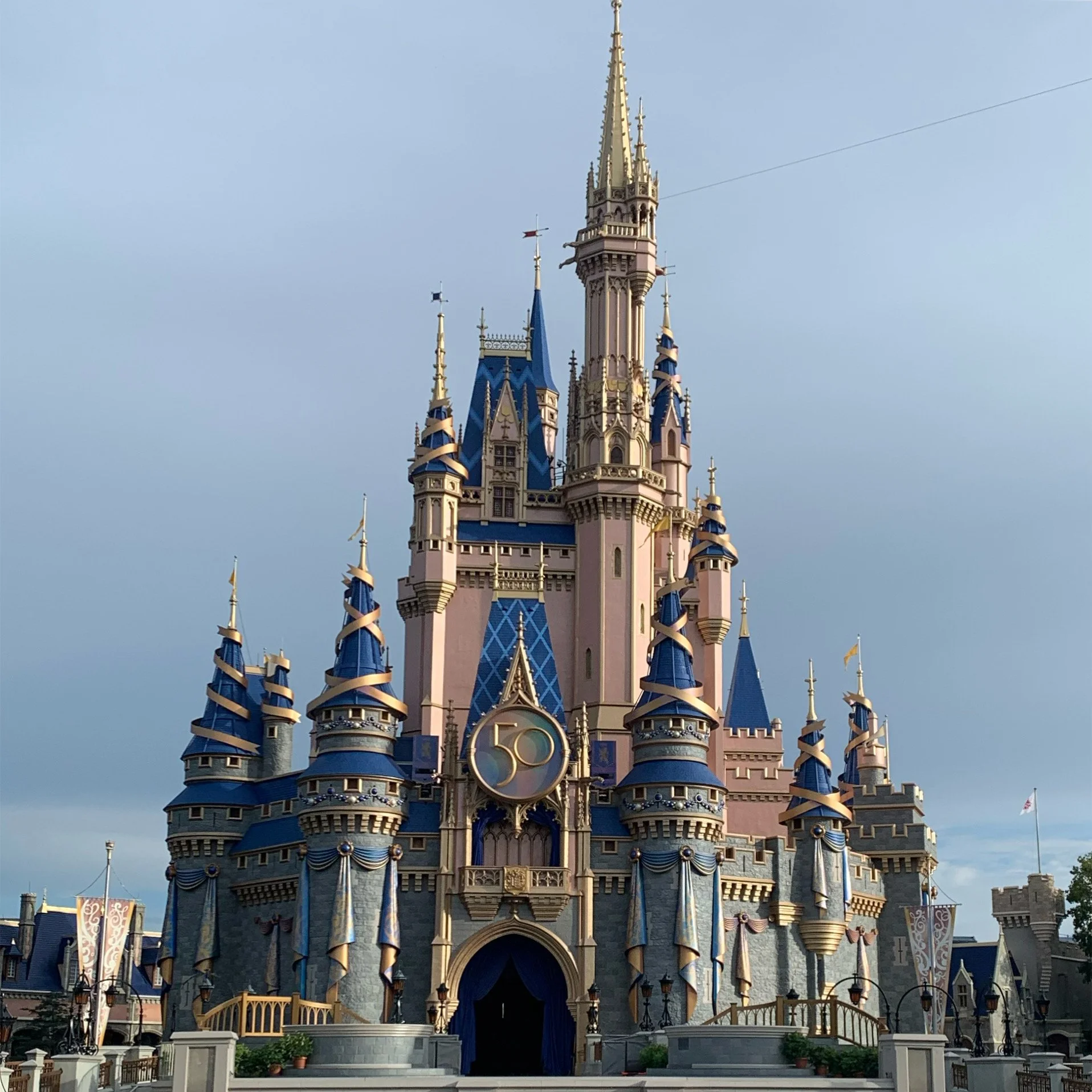 Cinderella Castle at Disney World theme park, featuring pink and blue turrets, ornate spires, and decorative banners against a clear blue sky.