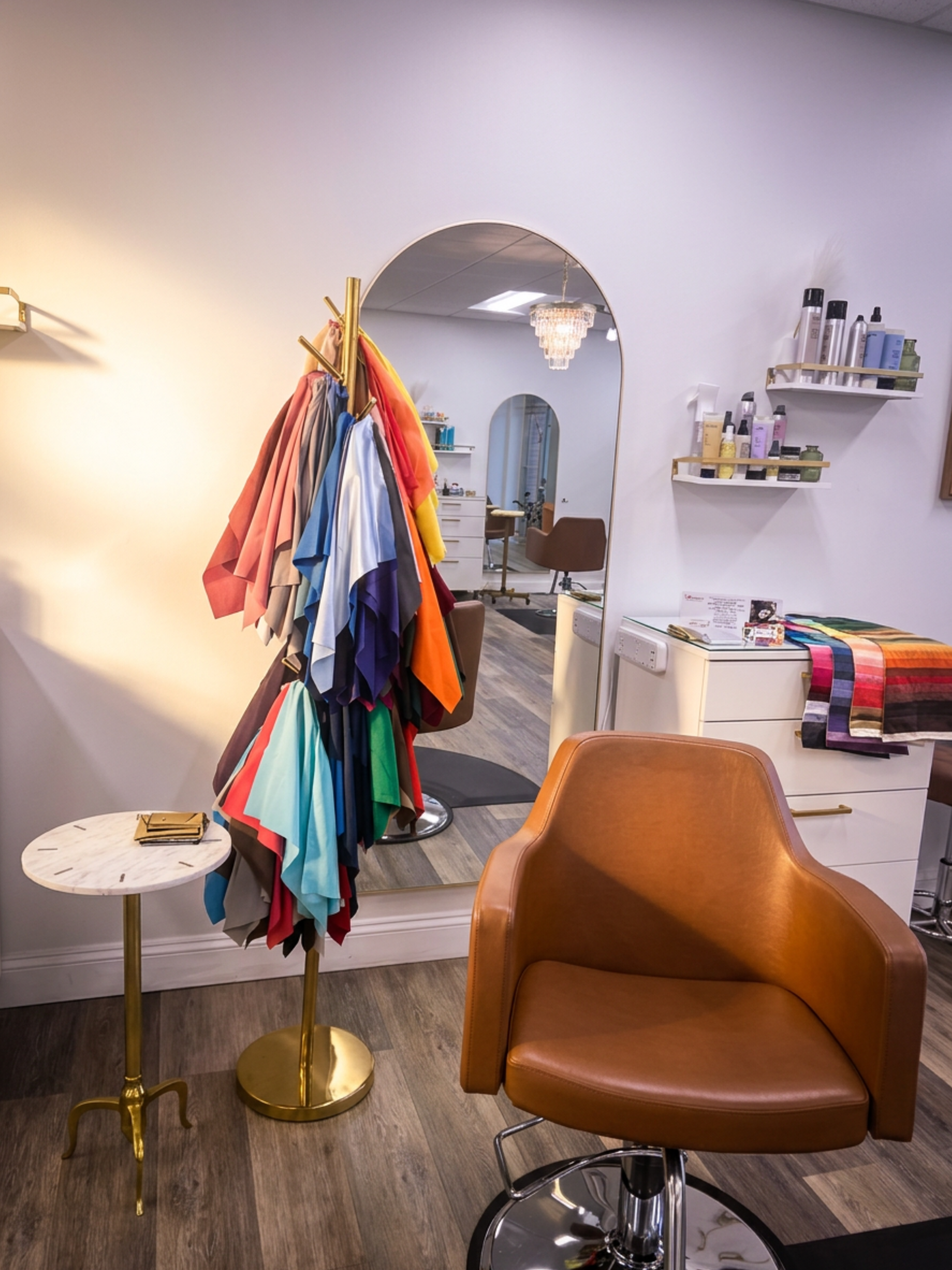 A salon and hair studio interior featuring a large mirror, a brown salon chair, a colorful fabric rack with various swatches, and shelves with hair products. Great for haircuts or color Analysis. Located in Columbia Maryland.