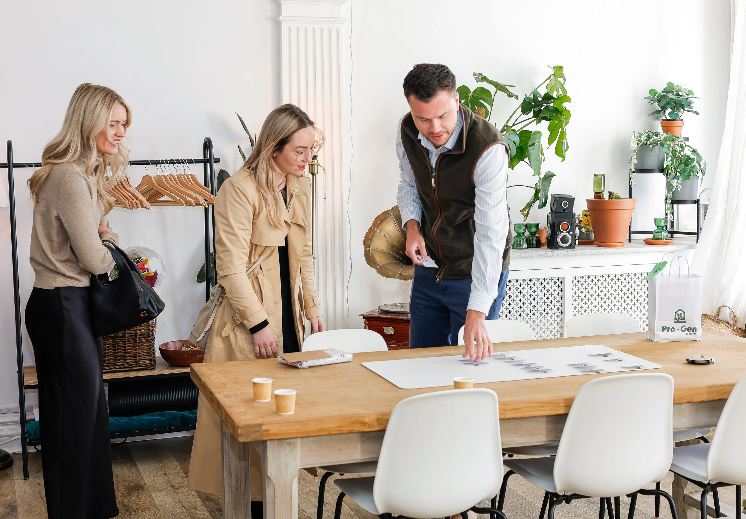 Four people gathered around a table in a brightly lit room with plants on the windowsill, engaging in a discussion.