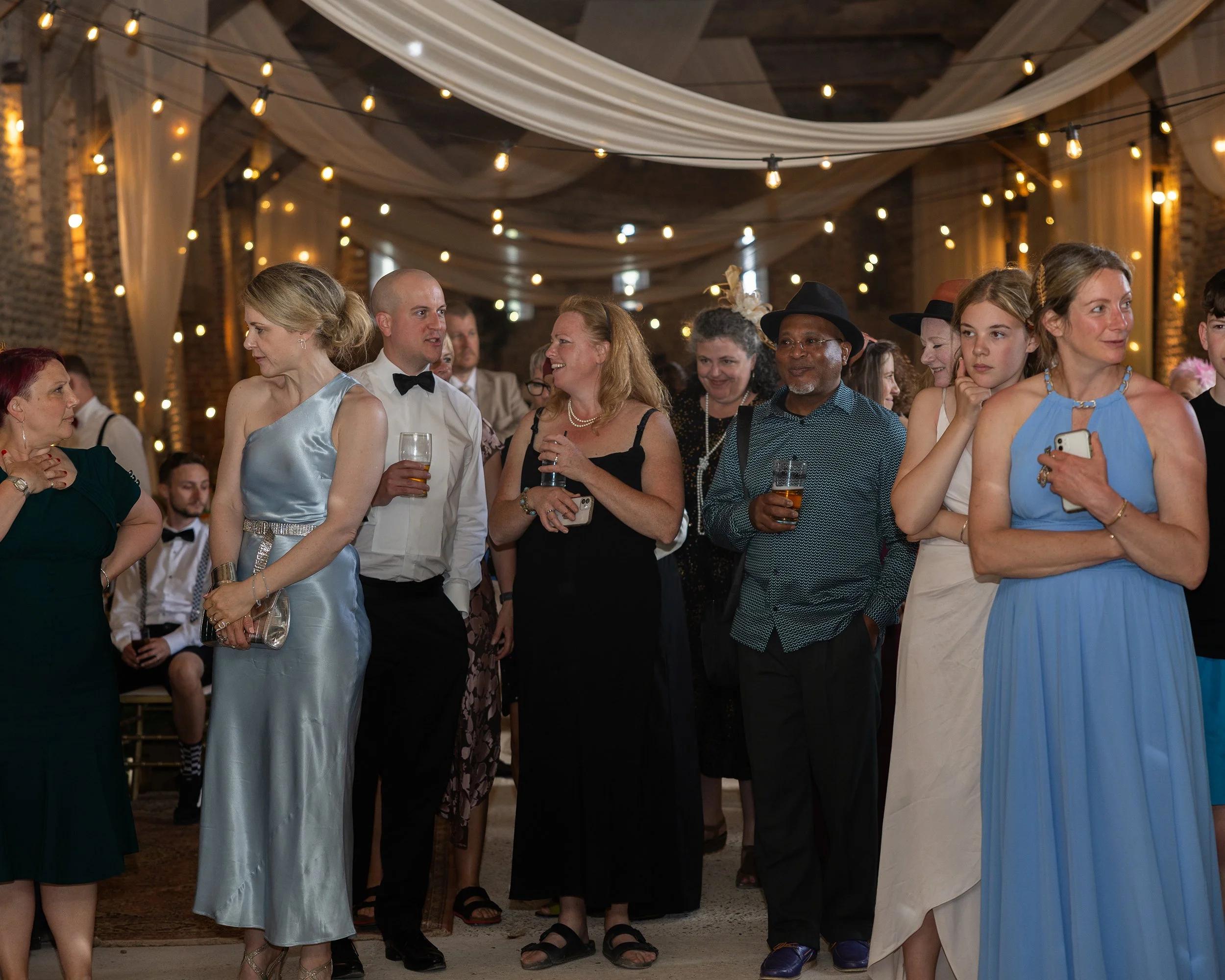 People dressed in formal attire attending an event in a decorated venue with string lights and draped fabric on the ceiling.