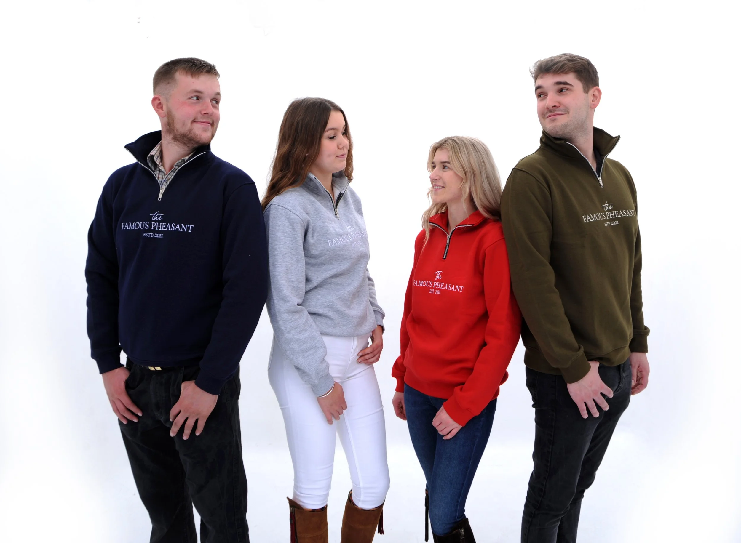 Four young adults standing in a line against a white background, wearing colorful sweatshirts with the text "the FAMOUS PHEASANT ESTD 2021" on them.