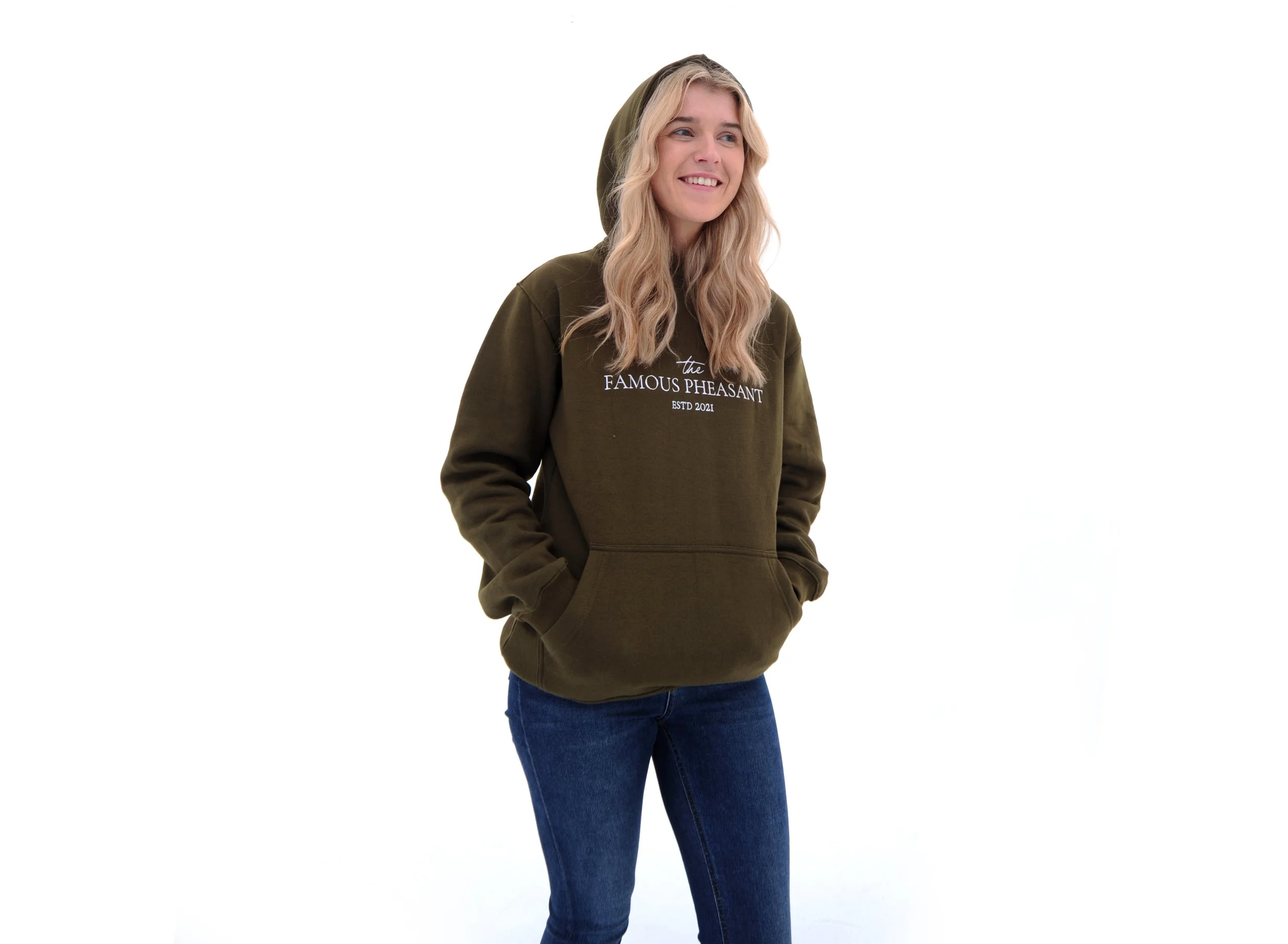 A woman wearing a green hoodie with the text 'the FAMOUS PHEASANT ESTD 2021', blue jeans, and a black headband is standing against a white background.