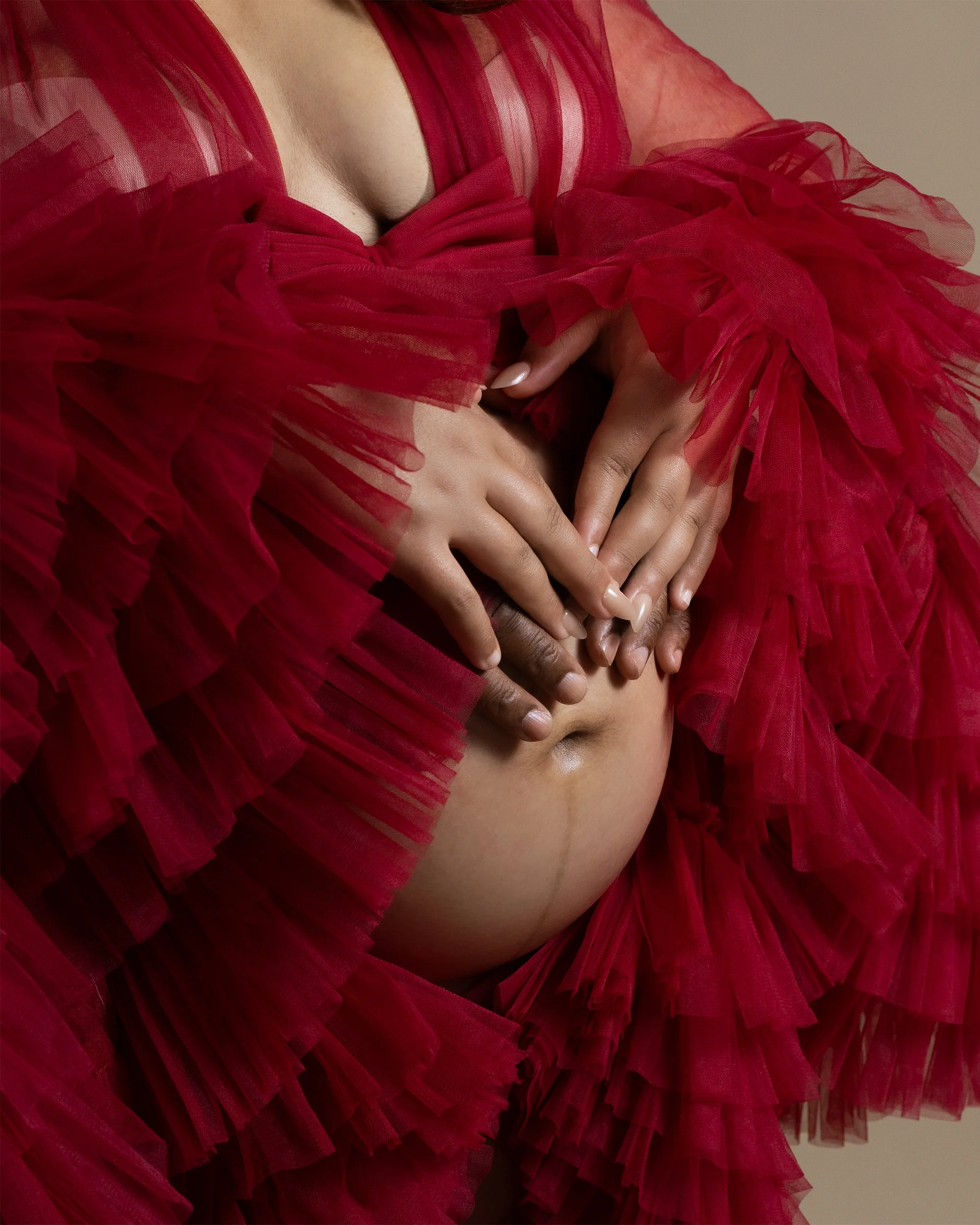 Close-up of a person wearing a red, ruffled, see-through dress, with hands gently touching their torso.