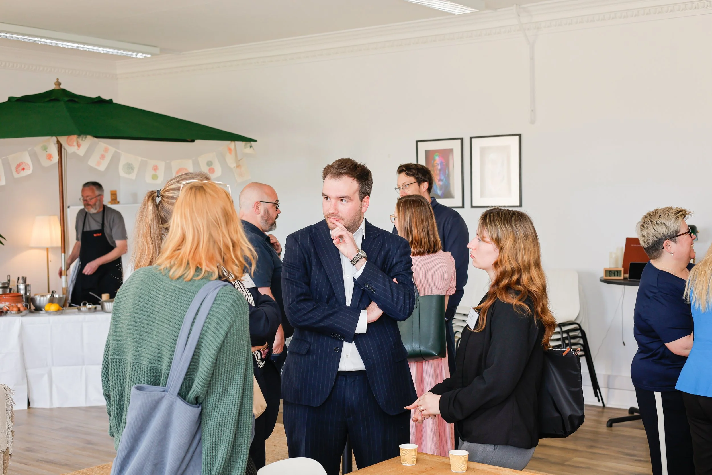 People networking and talking at an indoor event with a white table and a green holiday-themed umbrella in the background.