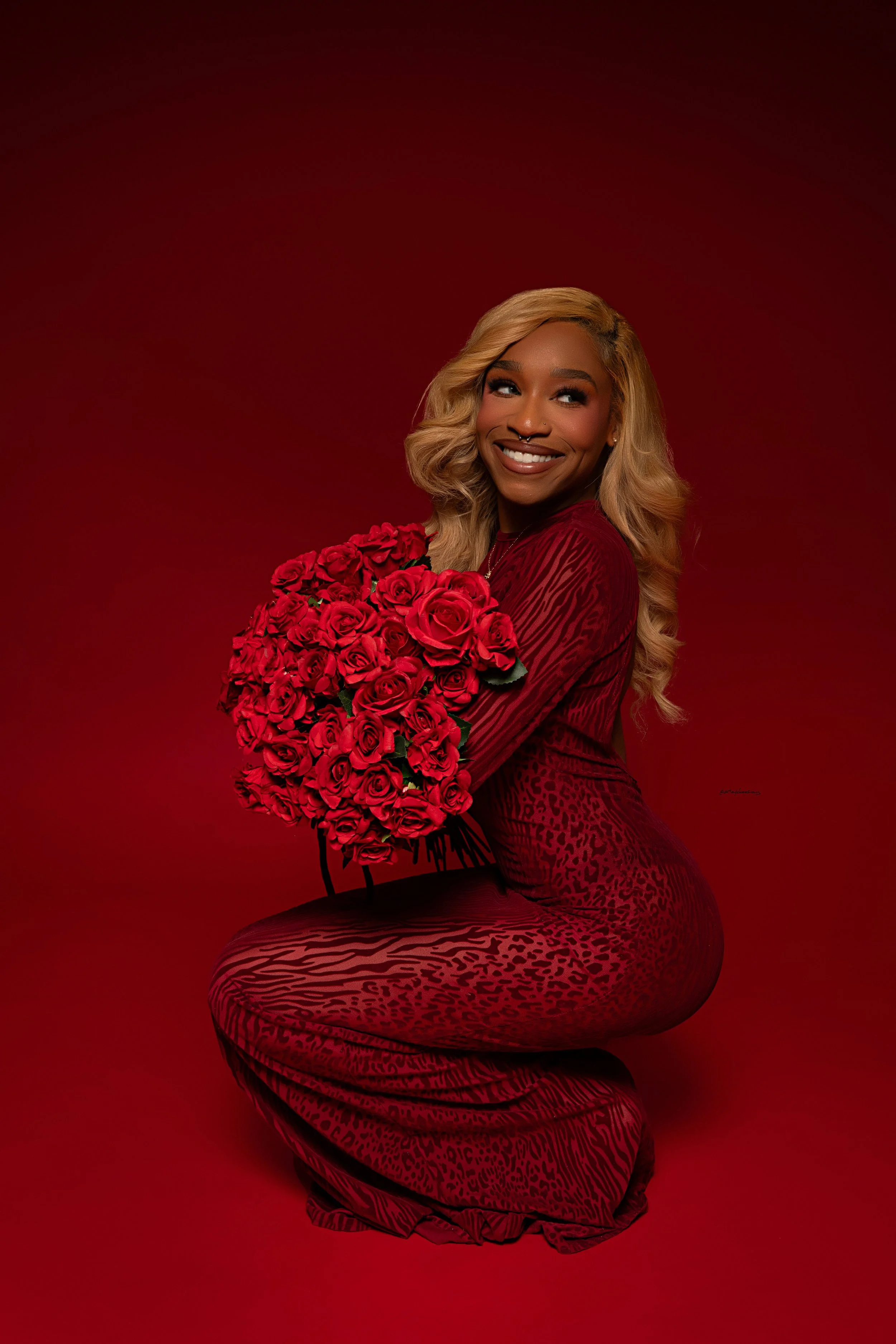 Woman wearing red dress on red background holding a bouquet of red roses