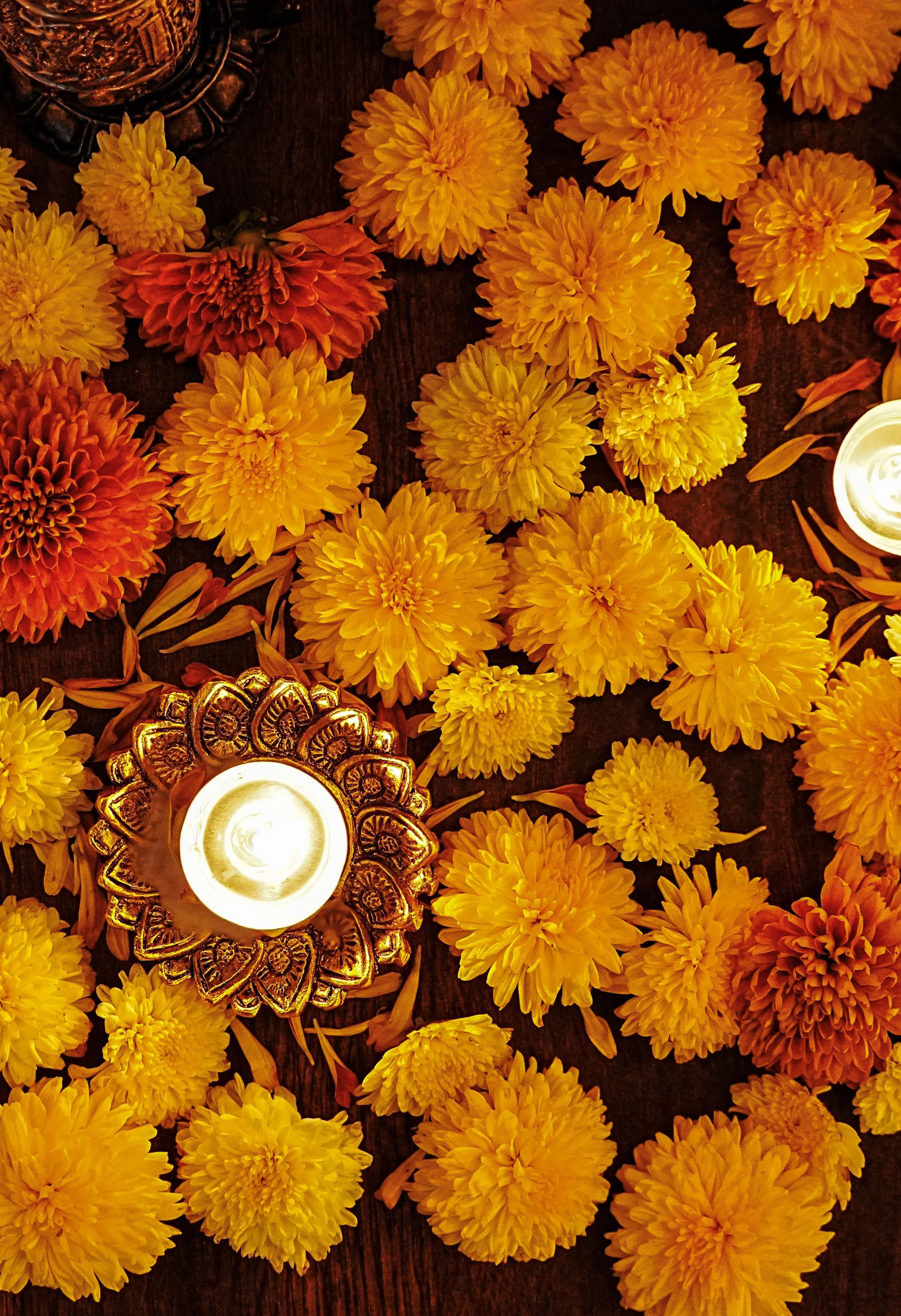 Yellow and orange marigold flowers arranged on a dark wooden surface with a lit tealight candle in a decorative gold holder.