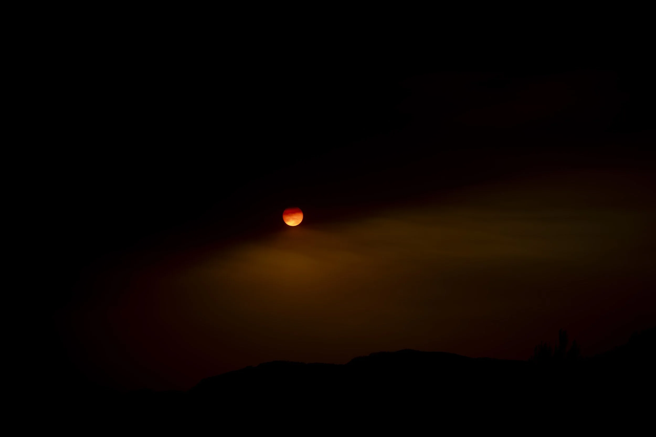 Sunset over the Els Ports mountains seen from a terrace in Benifallet, Spain, with hazy orange light over darkened hills